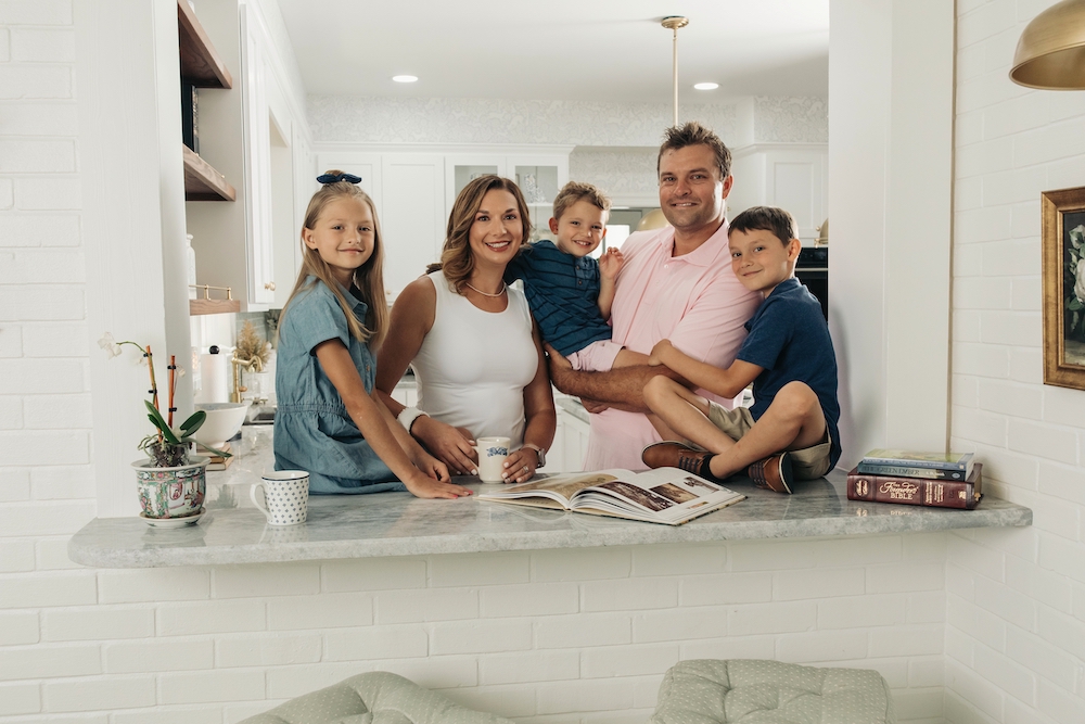 Robert Bortins' with his family, smiling at the camera from their kitchen counter