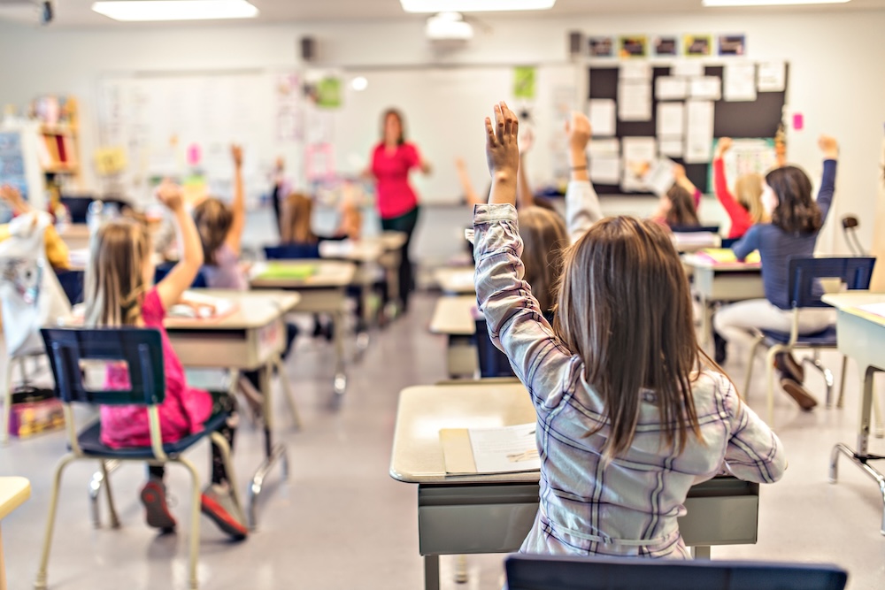 a classroom full of young students raising their hands